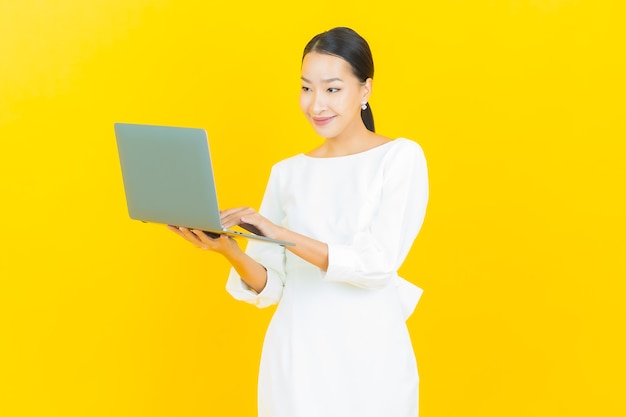 Retrato hermosa joven mujer asiática sonrisa con ordenador portátil en amarillo