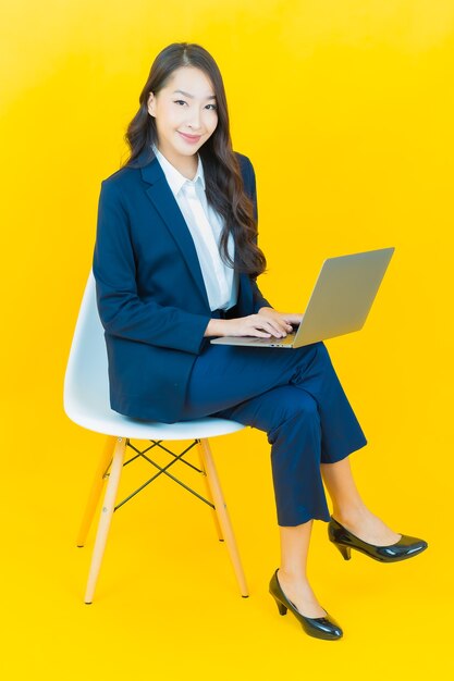 Retrato hermosa joven mujer asiática sonrisa con ordenador portátil en amarillo