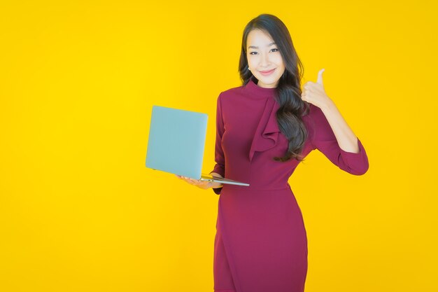 Retrato hermosa joven mujer asiática sonrisa con ordenador portátil en amarillo