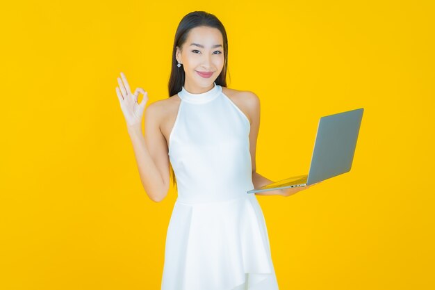 Retrato hermosa joven mujer asiática sonrisa con ordenador portátil en amarillo
