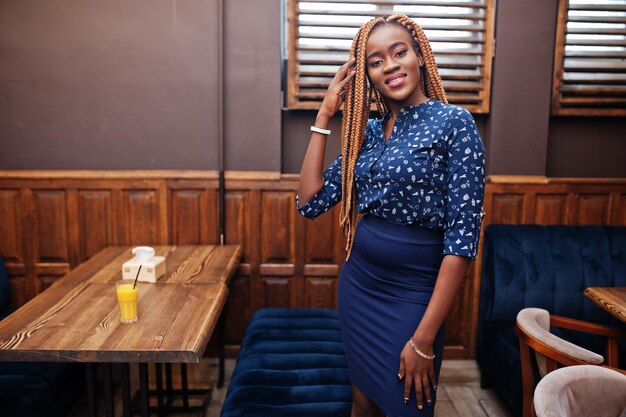 Retrato de una hermosa joven mujer de negocios africana con rastas en blusa azul y falda posada en un café