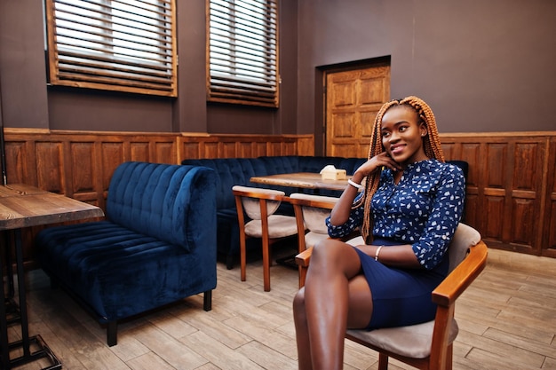 Retrato de una hermosa joven mujer de negocios africana vestida con blusa azul y falda sentada en un café