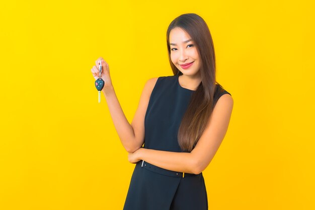 Retrato hermosa joven mujer de negocios asiática con llave de coche sobre fondo amarillo
