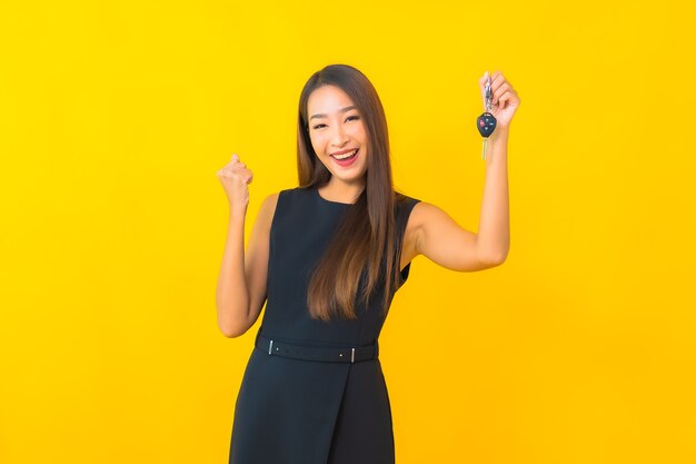 Retrato hermosa joven mujer de negocios asiática con llave de coche sobre fondo amarillo