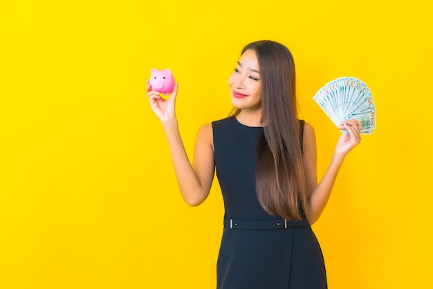 Retrato hermosa joven mujer de negocios asiática con mucho dinero en efectivo y dinero sobre fondo amarillo