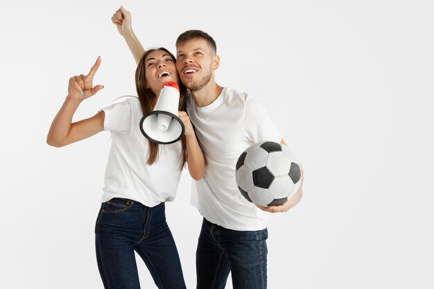 Retrato de la hermosa joven pareja de aficionados al fútbol o al fútbol en la pared blanca. Expresión facial, emociones humanas, publicidad, concepto deportivo. Mujer y hombre saltando, gritando, divirtiéndose.