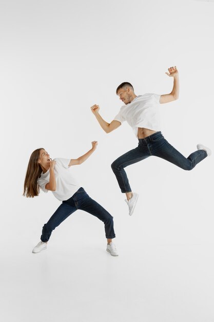 Retrato de la hermosa joven pareja aislado en la pared blanca. Expresión facial, emociones humanas, concepto publicitario. Copyspace. Mujer y hombre saltando, bailando o corriendo juntos.