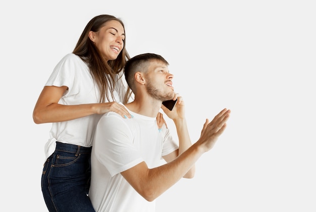 Retrato de la hermosa joven pareja aislado en la pared blanca. Expresión facial, emociones humanas, concepto publicitario. Hombre hablando por teléfono, la mujer quiere prestar atención a sí misma.