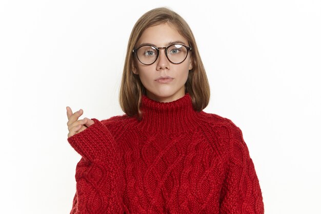 Retrato de una hermosa joven de pelo largo en anteojos y jersey marrón habiendo desconcertado la expresión facial confusa, haciendo gestos, pensando en algo, mirando