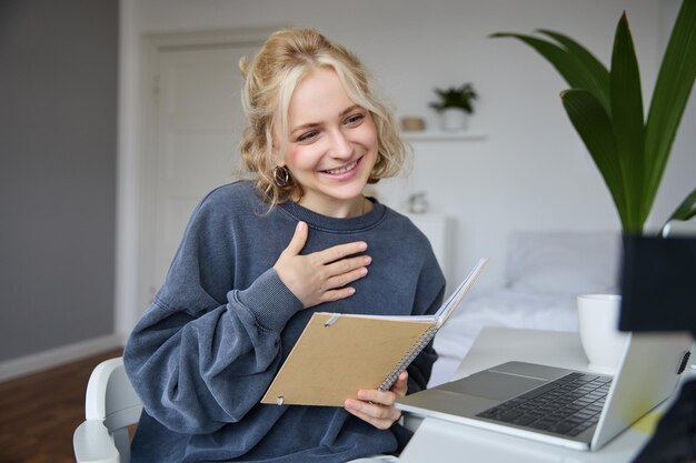 Retrato de una hermosa joven rubia sonriente que trabaja en una tarea desde casa en línea.