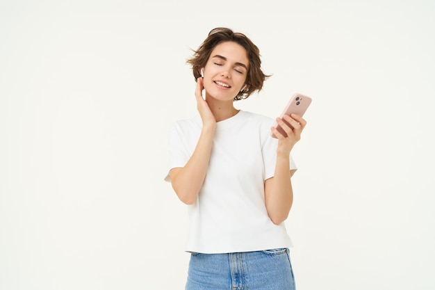 Foto gratuita retrato de una hermosa joven sonriente con auriculares inalámbricos pone música en los auriculares