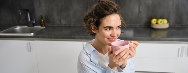 Retrato de una hermosa joven sonriente bebiendo café en la cocina con magia matutina y una taza de té