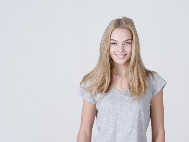 Retrato de una hermosa joven sonriente caucasion. Mujer con sonrisa dentuda. Atractiva chica rubia posa en el estudio con una camiseta casual