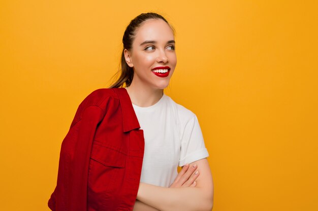 Retrato de hermosa joven sonriente con piel sana, labios rojos y cabello recogido juguetón mirando hacia arriba en la pared aislada, lugar para el texto