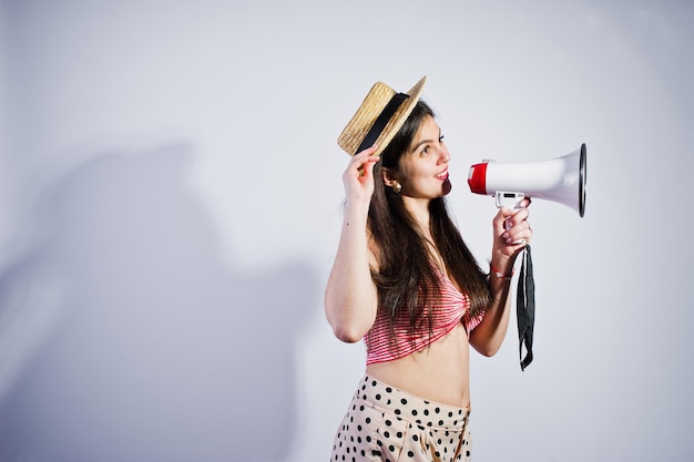 Retrato de una hermosa joven en traje de baño y sombrero habla por megáfono en el estudio