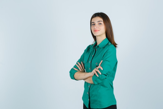 Retrato de hermosa jovencita sosteniendo los brazos cruzados en camisa verde y mirando orgullosa vista frontal