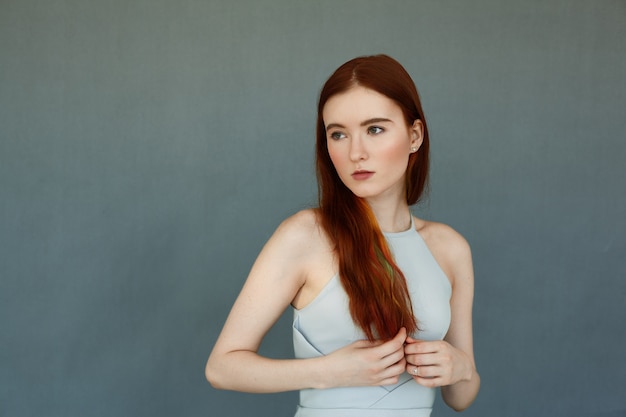 Retrato de la hermosa modelo femenina con cabello largo rojo y hermosos ojos verdes contra la pared de ladrillo azul. atractiva mujer joven mirando a otro lado con expresión pensativa y soñadora