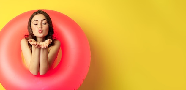 Foto gratuita retrato de hermosa modelo femenina posando con anillo de playa de natación rosa enviando beso de aire mwah coqueto