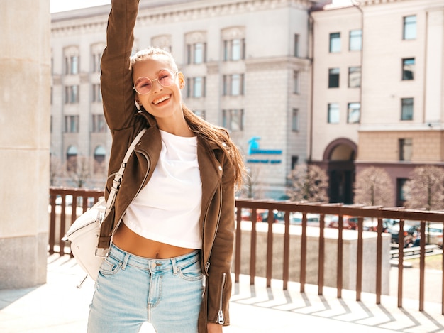 Retrato de la hermosa modelo morena sonriente vestida con ropa de verano hipster chaqueta. . Levantando sus manos