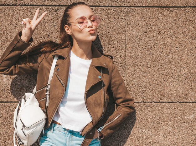 Retrato de la hermosa modelo morena sonriente vestida con ropa de verano hipster chaqueta mostrando signo de paz