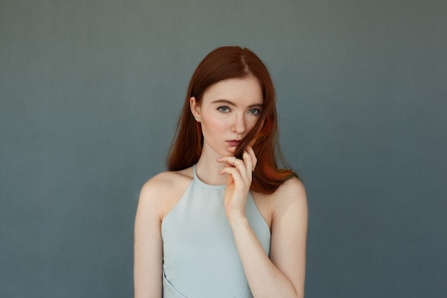 Retrato de hermosa modelo de mujer joven pelirroja con ojos verdes y maquillaje de la naturaleza, tocando su cabello largo mirando con expresiones serias