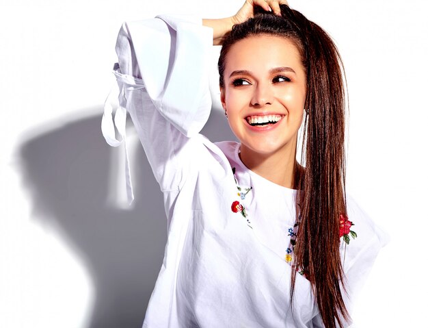 Retrato de la hermosa modelo de mujer morena caucásica sonriente en blusa blanca y elegantes jeans de verano con estampado de flores