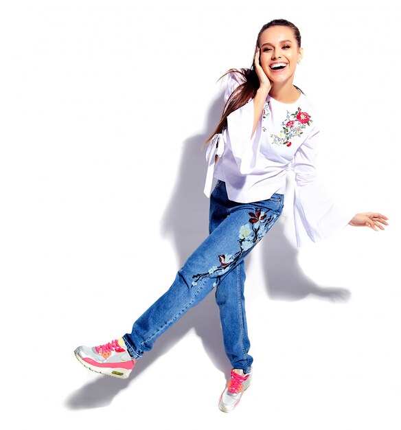 Retrato de la hermosa modelo de mujer morena caucásica sonriente en blusa blanca y verano elegante blue jeans con flores