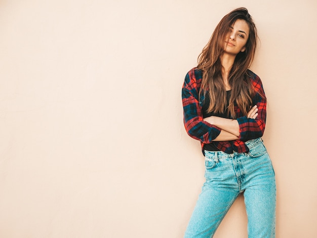 Foto gratuita retrato de hermosa modelo. mujer sexy vestida con jeans y camisa a cuadros de verano hipster. chica de moda posando junto a la pared en la calle