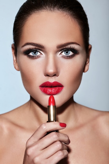 Retrato de la hermosa modelo de niña con maquillaje de noche con pomada roja en las manos