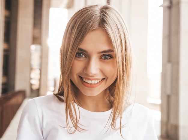 Retrato de la hermosa modelo rubia sonriente vestida con ropa hipster de verano. Chica de moda posando en el fondo de la calle. Mujer divertida y positiva