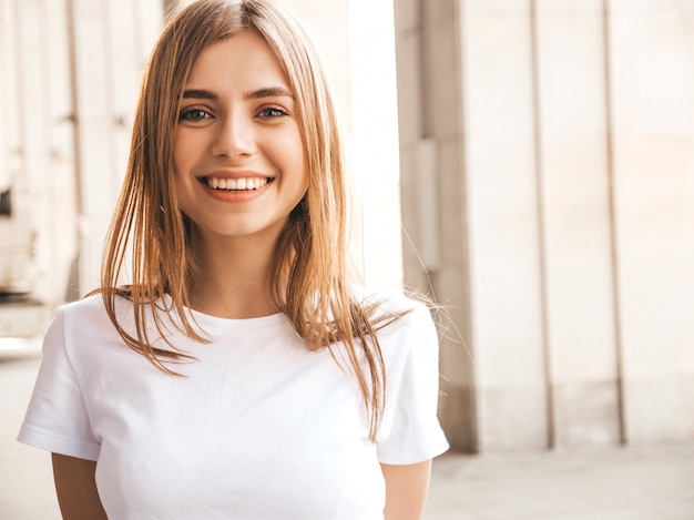 Retrato de la hermosa modelo rubia sonriente vestida con ropa hipster de verano. Chica de moda posando en el fondo de la calle. Mujer divertida y positiva