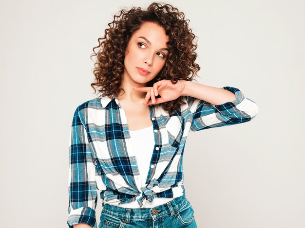 Retrato de hermosa modelo sonriente con peinado afro rizos vestido con ropa hipster de verano. Chica despreocupada sexy posando en estudio sobre fondo gris. Mujer divertida y positiva de moda