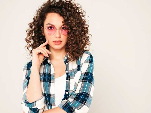 Retrato de hermosa modelo sonriente con peinado afro rizos vestido con ropa hipster de verano. Chica despreocupada sexy posando en estudio sobre fondo gris. Mujer divertida y positiva de moda