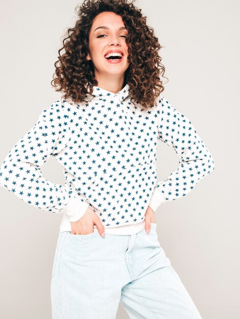 Retrato de hermosa modelo sonriente con peinado afro rizos vestido con ropa hipster de verano. Chica despreocupada sexy posando en estudio sobre fondo gris. Mujer divertida y positiva de moda