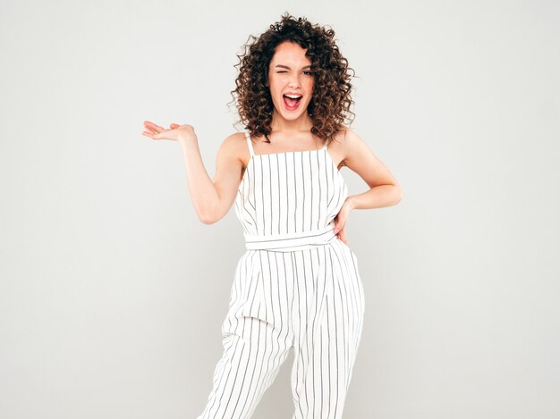 Retrato de hermosa modelo sonriente con peinado afro rizos vestido con ropa hipster de verano. La mujer de moda muestra algo en su mano