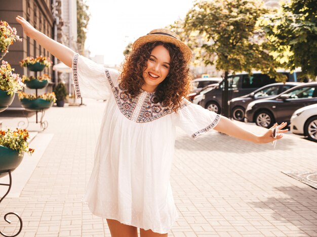 Retrato de hermosa modelo sonriente con peinado afro rizos vestido con vestido blanco hipster de verano.