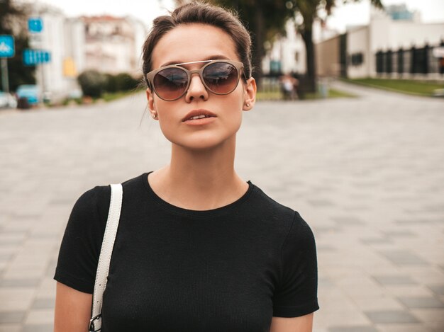 Retrato de hermosa modelo sonriente vestida con ropa de verano. Chica de moda posando en la calle con gafas de sol. Mujer divertida y positiva divirtiéndose