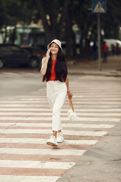 Retrato de hermosa morena. Modelo en ciudad de verano. Mujer camina con teléfono móvil.