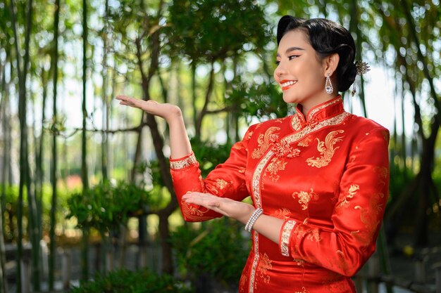 Retrato hermosa mujer asiática en un cheongsam chino extiende su palma como espacio en blanco para insertar una imagen para publicidad