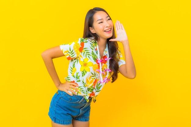 Retrato de hermosa mujer asiática joven con camisa colorida y diciendo un secreto en la pared amarilla