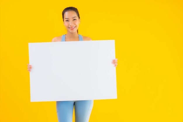 Retrato hermosa mujer asiática joven desgaste ropa deportiva mostrar cartelera blanca vacía en amarillo