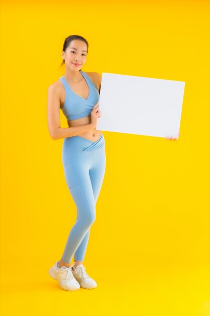 Retrato hermosa mujer asiática joven desgaste ropa deportiva mostrar cartelera blanca vacía en amarillo