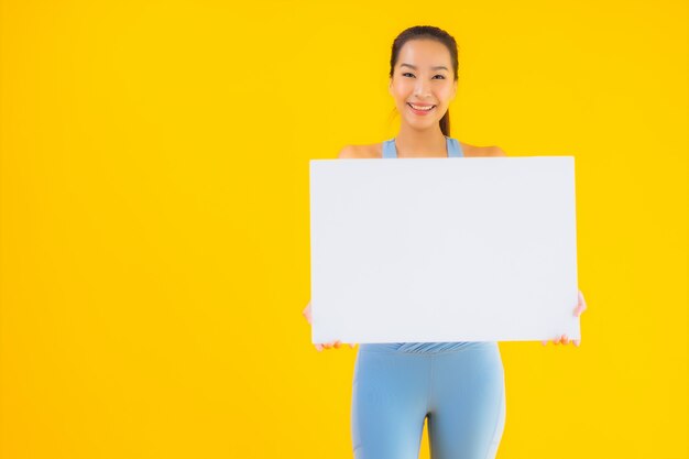 Retrato hermosa mujer asiática joven desgaste ropa deportiva mostrar cartelera blanca vacía en amarillo