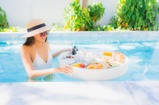 Retrato hermosa mujer asiática joven feliz sonrisa con desayuno flotante en bandeja en la piscina