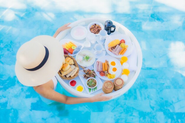 Retrato hermosa mujer asiática joven feliz sonrisa con desayuno flotante en bandeja en la piscina