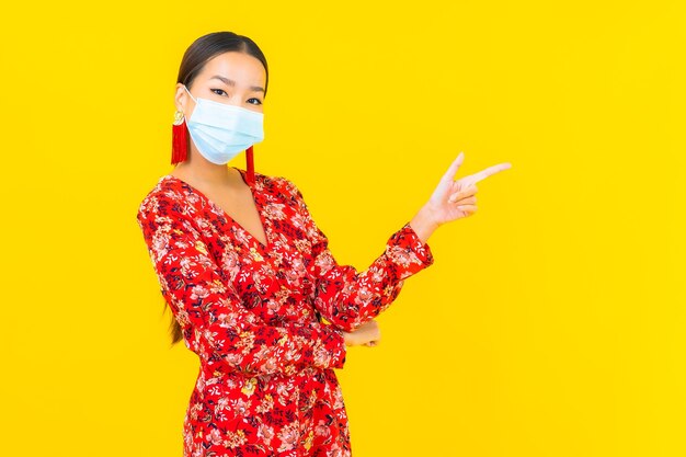 Retrato hermosa mujer asiática joven con máscara para proteger el virus corona o covid19 en la pared amarilla