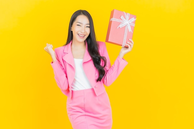 Retrato hermosa mujer asiática joven sonrisa con caja de regalo roja en la pared de color amarillo