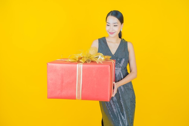 Retrato hermosa mujer asiática joven sonrisa con caja de regalo roja sobre amarillo