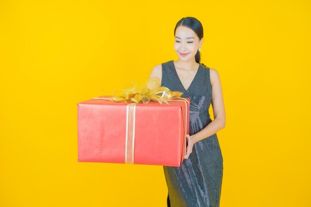 Retrato hermosa mujer asiática joven sonrisa con caja de regalo roja sobre amarillo