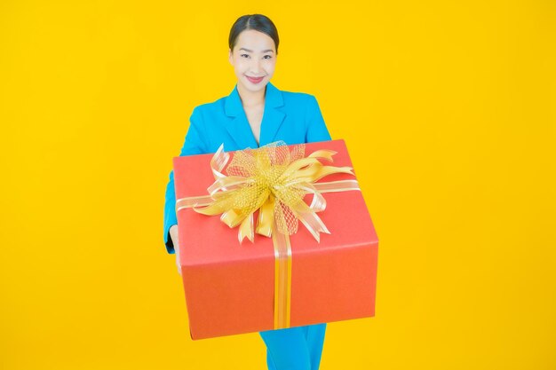 Retrato hermosa mujer asiática joven sonrisa con caja de regalo roja sobre amarillo